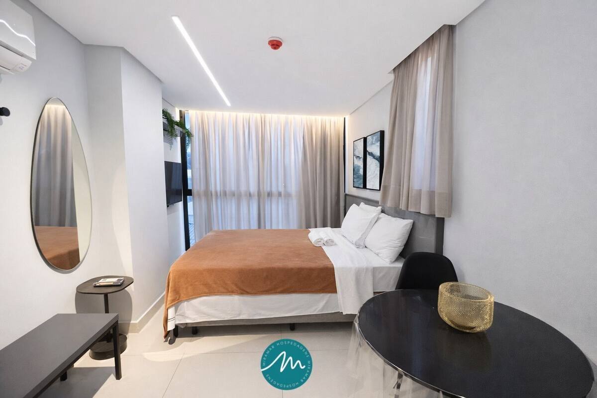 A modern hotel room with a bed, bedside table, chair, and a round table with a woven basket.