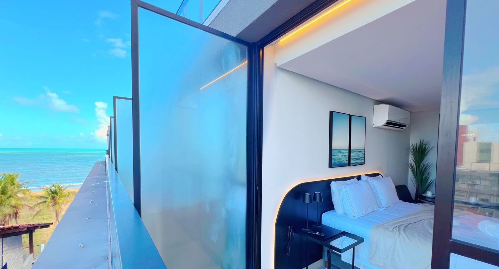 A modern hotel room with a large glass balcony, a bed, a nightstand, and a wall-mounted air conditioning unit.