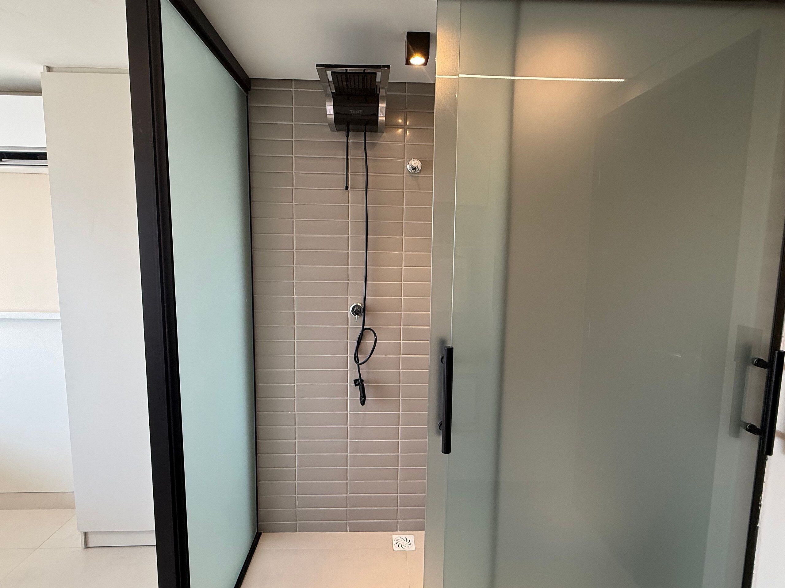 A modern bathroom with a glass shower enclosure, a visible water heater, and a tiled wall.