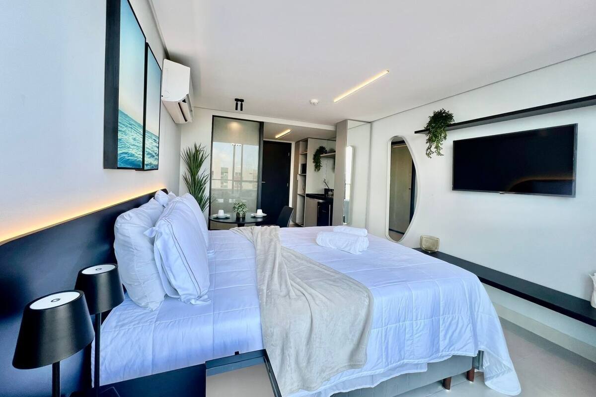 A modern hotel room with a large bed, bedside lamps, a flat-screen TV, a mirror, and a small table with a plant.