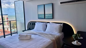 A hotel room with a bed, a nightstand, a table with a plant, and a view of the ocean. - Alta Garden (João Pessoa)