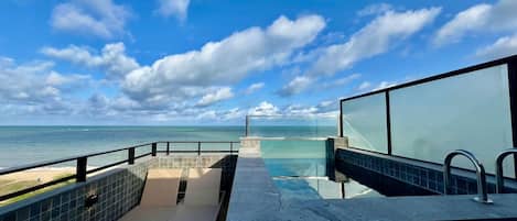 A pool area with a view of the ocean, a glass barrier, and a tiled floor.