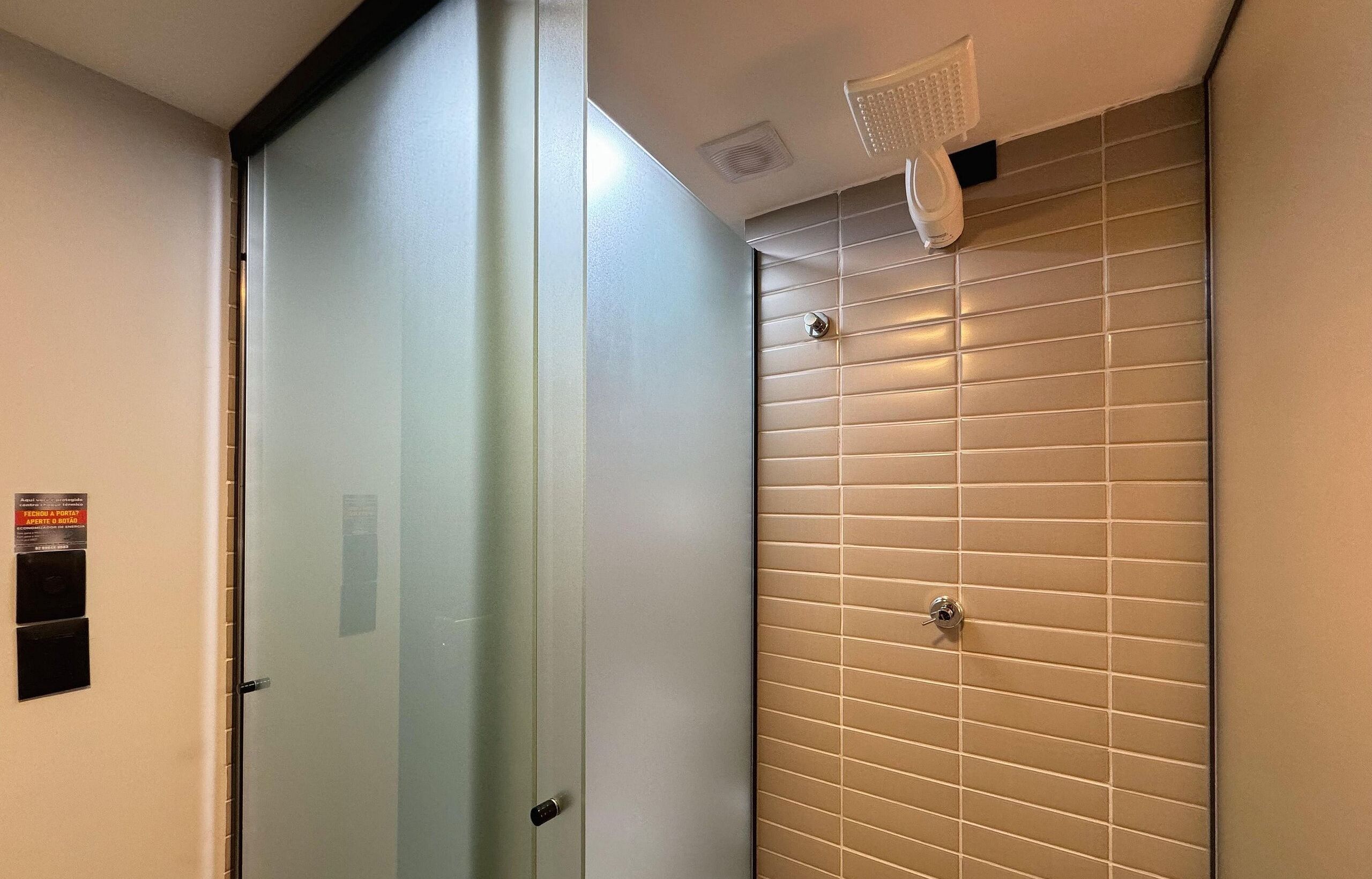 A bathroom with a frosted glass door, a tiled wall, and a ceiling-mounted light fixture.