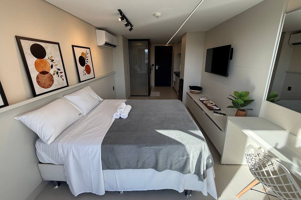 A modern hotel room with a bed, a desk, a TV, and artwork on the walls.