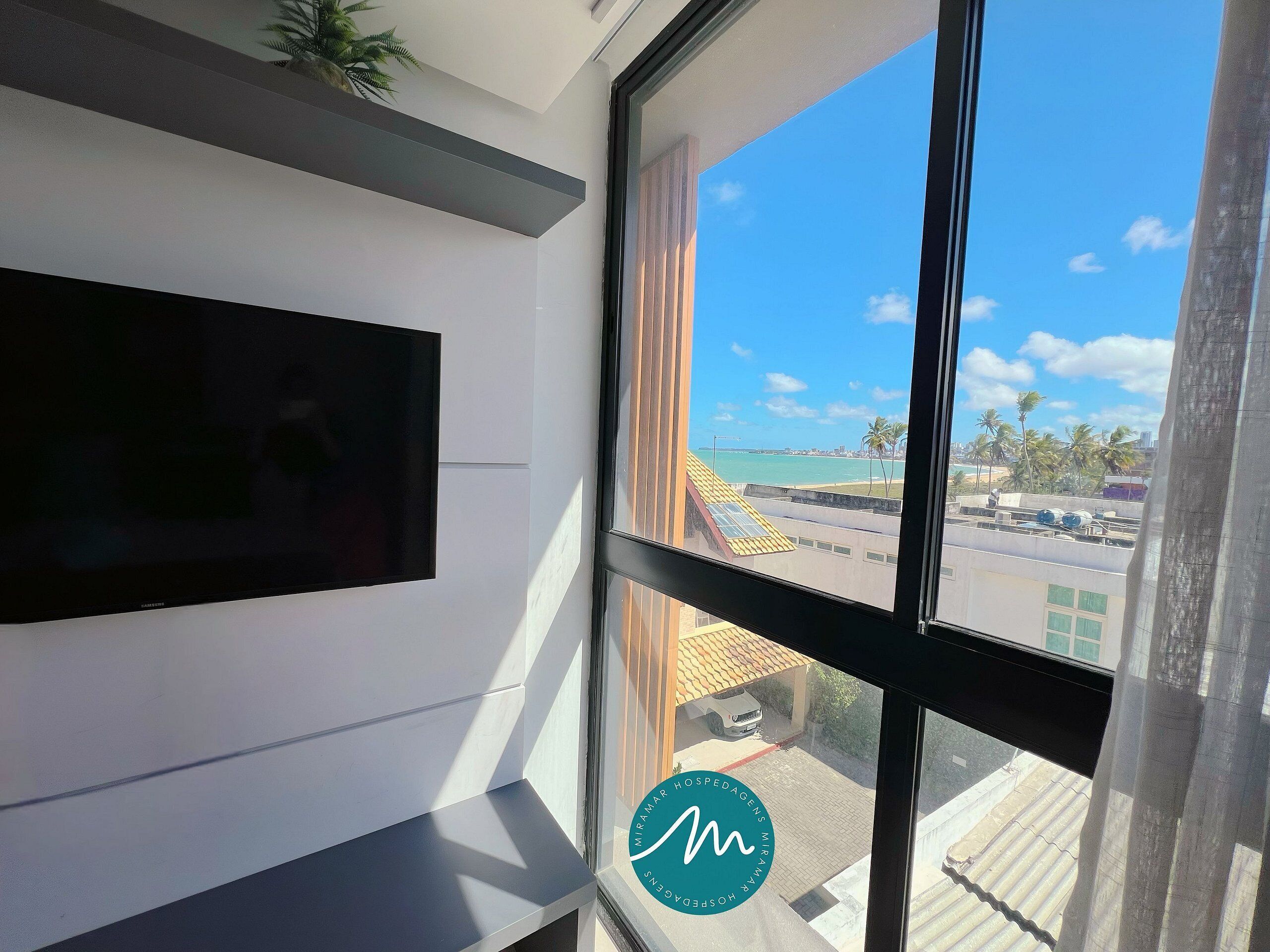 A room with a large window, a flat-screen TV mounted on the wall, and a logo on the window frame.