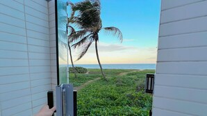 A view through a window with a door handle, palm trees, and a beach in the background. - Alta Garden (João Pessoa)