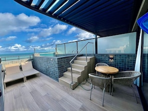 A modern outdoor deck with a pool, seating area, and a view of the ocean.