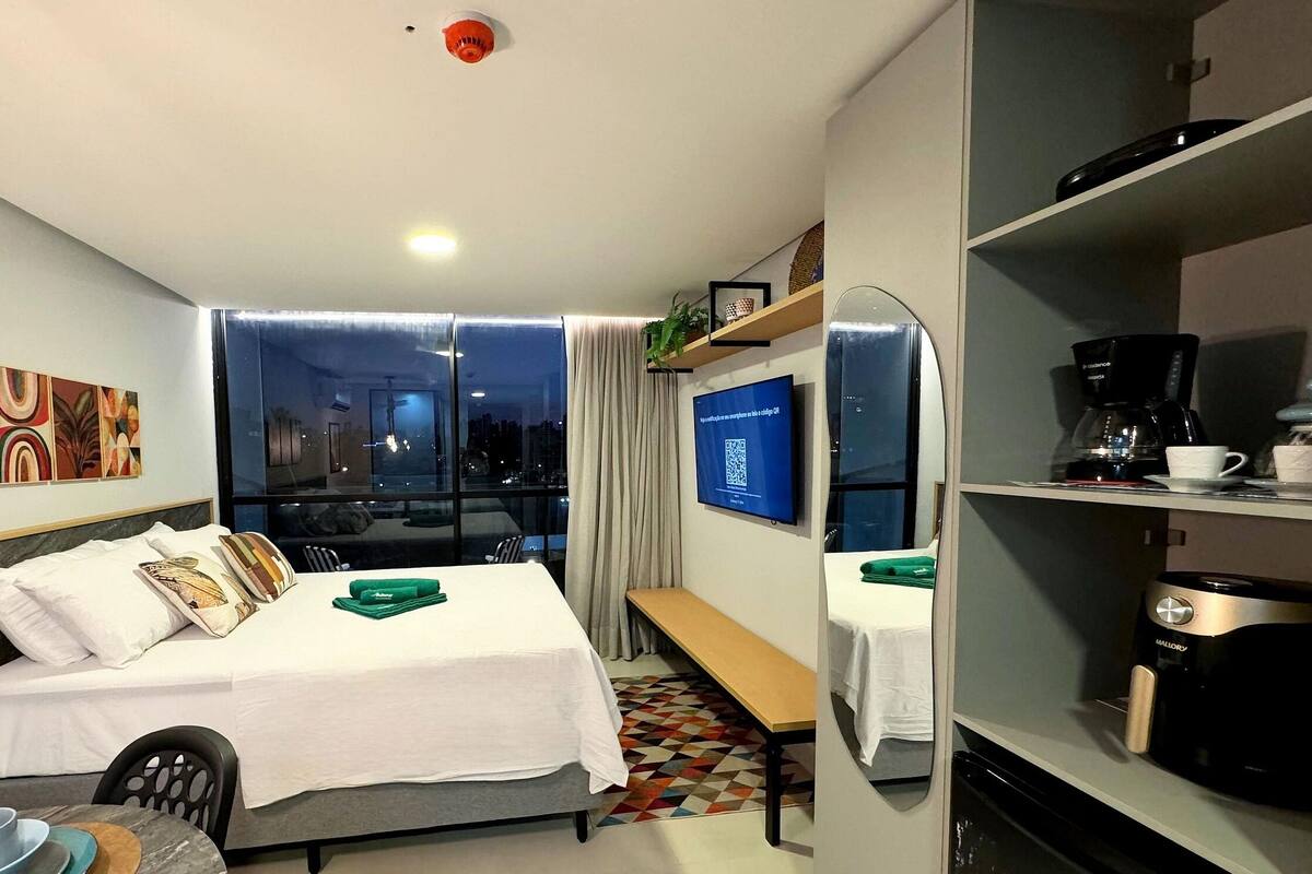 A hotel room with a bed, a desk, a coffee machine, a TV, and a window with a city view.