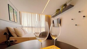 A modern hotel room with a bed, a table with two wine glasses, a TV, and a window with curtains. - Alta Garden (João Pessoa)