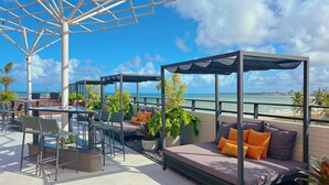 A rooftop terrace with seating areas, planters, and a view of the ocean. - Alta Garden (João Pessoa)