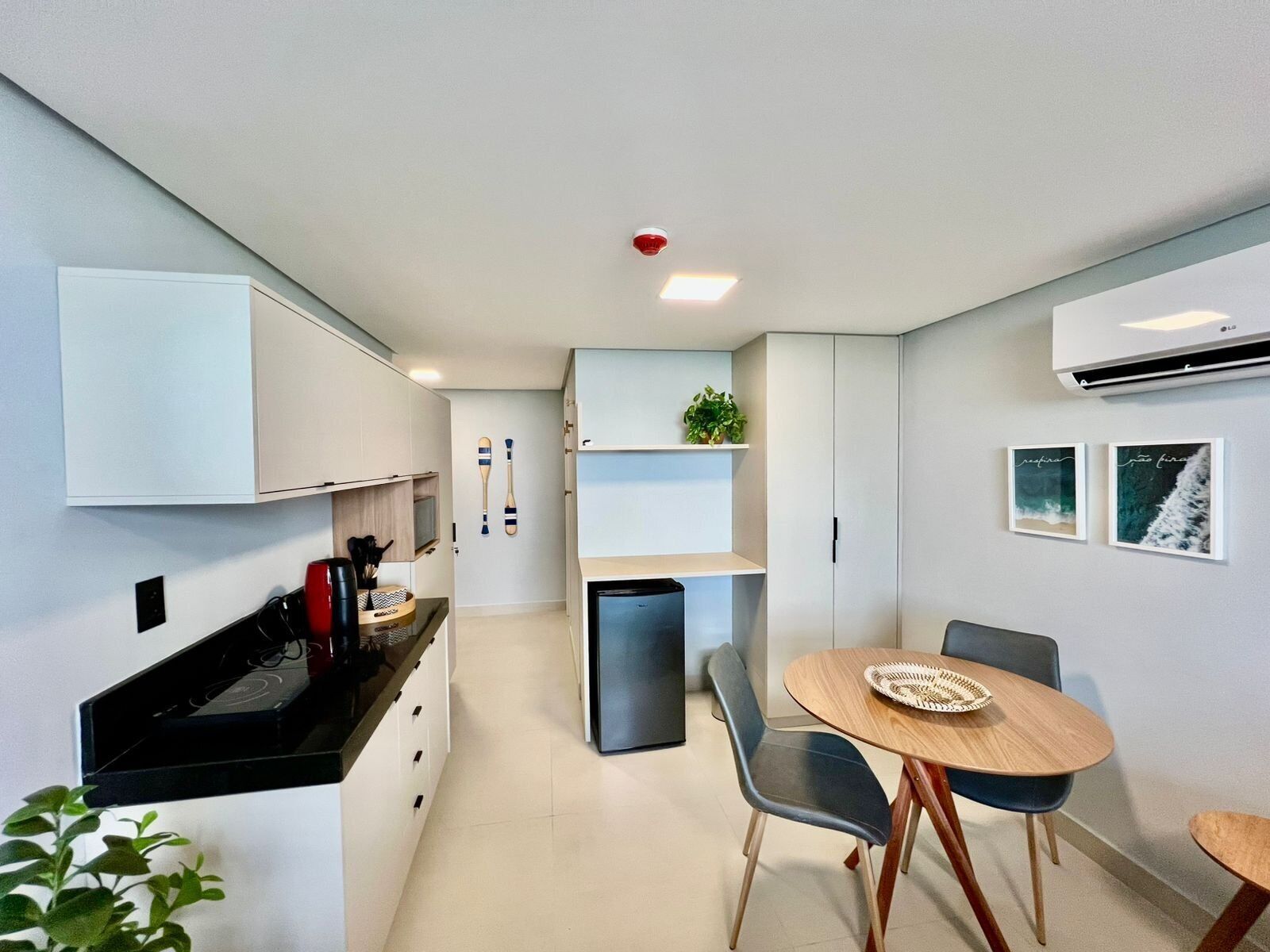 A modern kitchen with white cabinets, a black countertop, a small refrigerator, and a dining area with a wooden table and chairs.