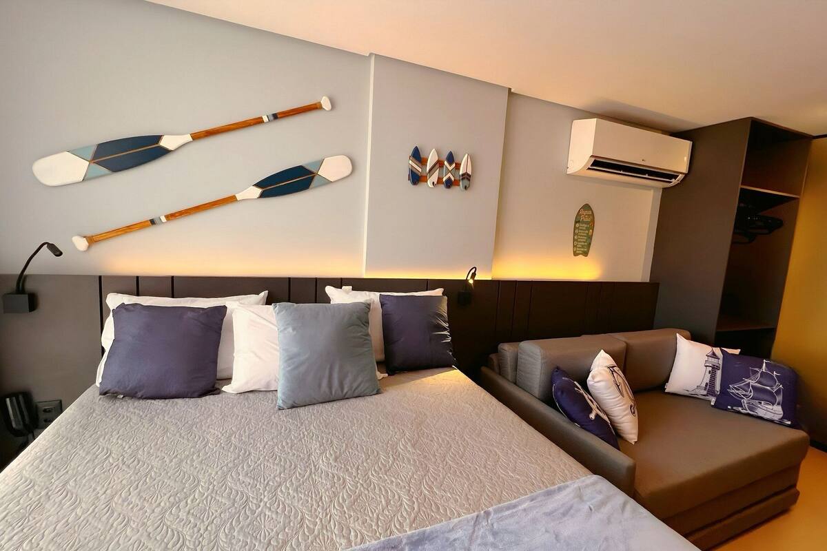 A hotel room with a bed, a sofa, a wall-mounted air conditioner, and decorative items including paddles and a menu board.