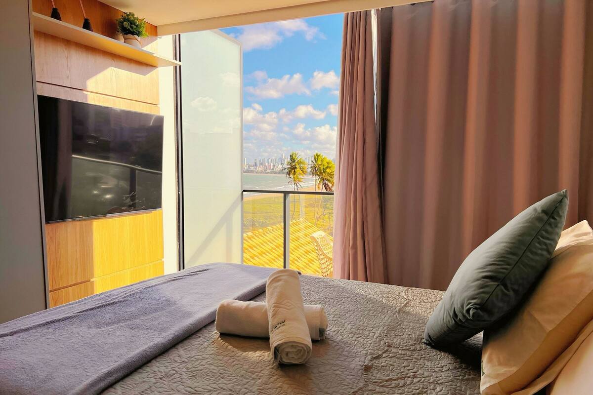 A hotel room with a bed, a view of the cityscape, and a balcony with a railing.
