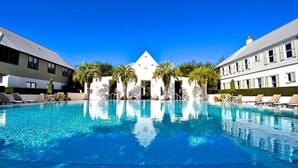 A swimming pool with lounge chairs and palm trees, surrounded by buildings with a classic architectural style. - Rosemary Beach Rooftop Heated Pool w/ Carriage House (Rosemary Beach)