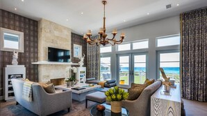 A modern living room with a fireplace, comfortable seating, a large TV, and a view of the ocean. - Rosemary Beach Rooftop Heated Pool w/ Carriage House (Rosemary Beach)
