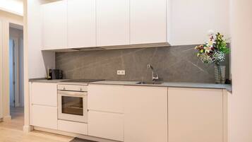 Eine moderne Küche mit weißen Schränken, einem eingebauten Backofen, einer Edelstahl-Spüle und einer Marmor-Spritzschutzwand.