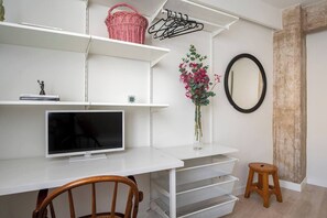 A modern living space with a flat-screen TV, white shelving, a wooden chair, a small stool, and a vase with flowers. - Apartamento Vargas 73. (Santander)