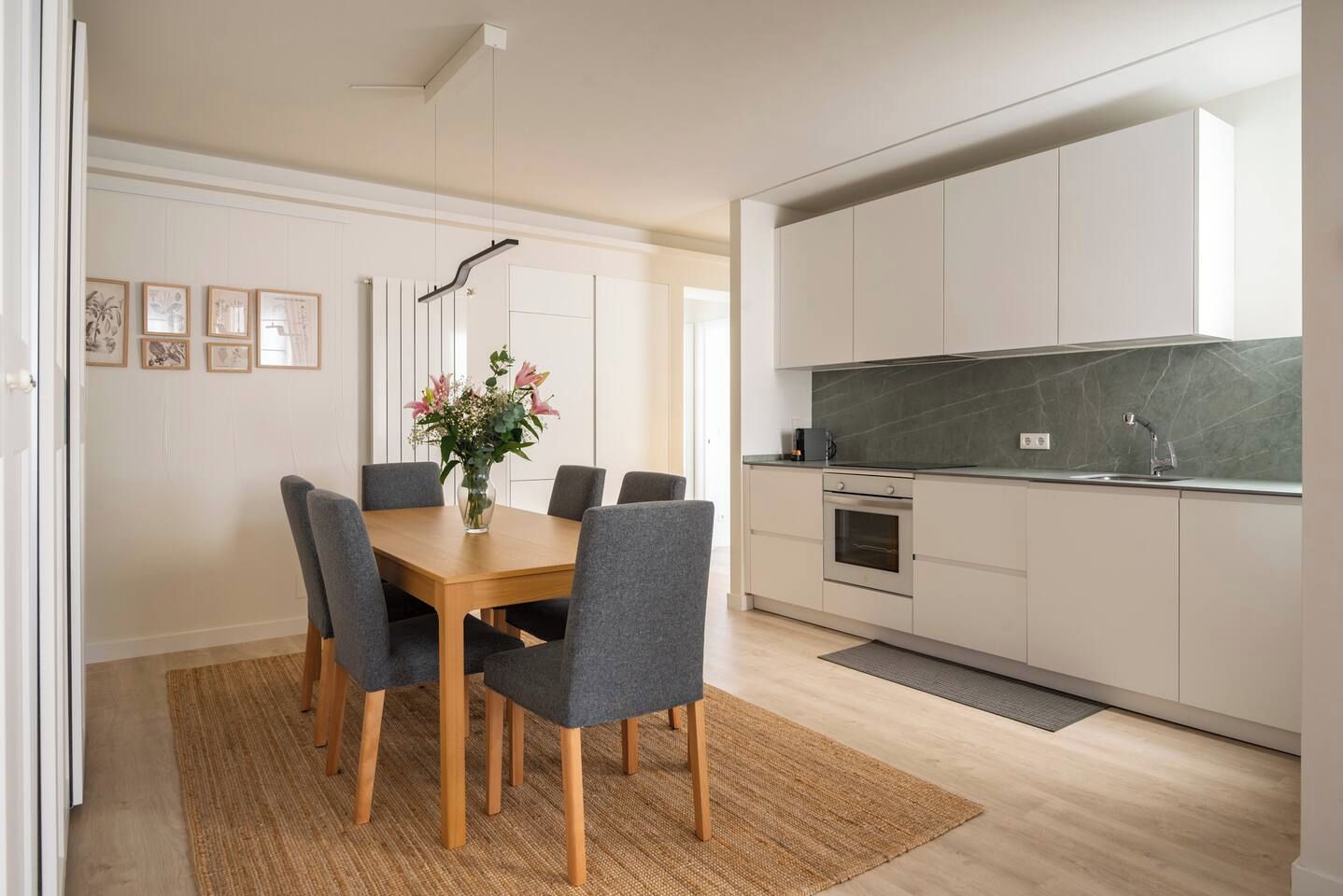 Eine moderne Küche mit einer zentralen Kochinsel, einem Essbereich mit Holztisch und grauen Stühlen sowie einer Küchenarbeitsfläche mit Spüle und Herd.
