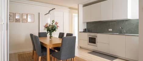 A modern kitchen with a central island, a dining area with a wooden table and grey chairs, and a kitchen counter with a sink and stove.