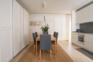 A modern kitchen with white cabinets, a wooden dining table, and a vase with flowers. - Apartamento Vargas 73. (Santander)