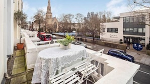 A balcony with a table and chairs, overlooking a street with a church and a primary school building. - Chic & Cosy Flat, 4-Min Walk to Pimlico Tube. Pet Friendly (London)