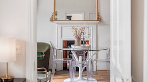 A dining area with a glass table and chairs, a white fireplace, and a gold-framed mirror above. - Chic & Cosy Flat, 4-Min Walk to Pimlico Tube. Pet Friendly (London)
