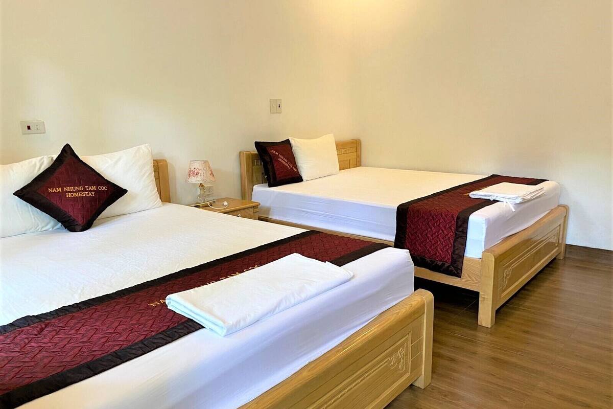 Une chambre d’hôtel avec deux lits simples, chacun recouvert d’une couvre-lit rouge et blanche assortie aux oreillers. Il y a un banc en bois au pied des lits, ainsi qu’une petite table de chevet avec une lampe.