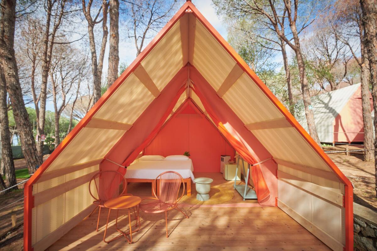 A triangular tent with a bed, a chair, and a small table.