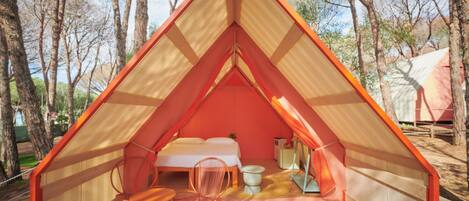 A triangular tent with a bed, a chair, and a small table.