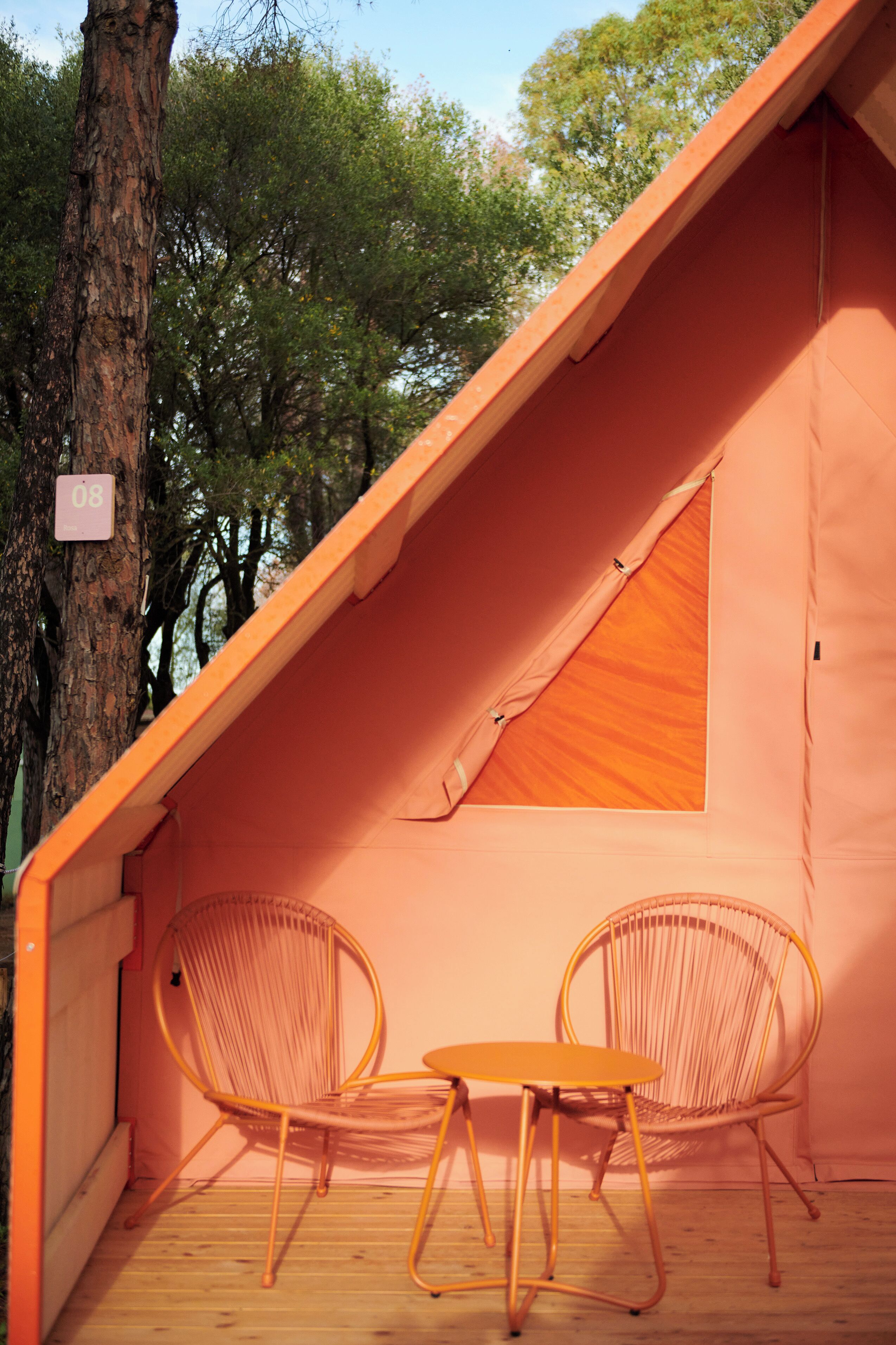 A cozy, orange-roofed cabin with two wicker chairs and a small table, surrounded by trees.