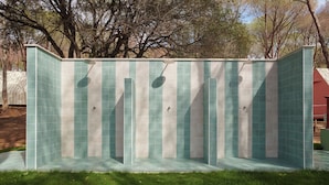A covered outdoor shower area with a tiled floor and walls, surrounded by grass and trees. - LAVITA Camp - Cagliari Villasimius (Quartu Sant'Elena)