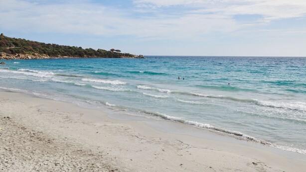 A beach with clear blue water, sandy shore, and a hilly landscape in the background. - LAVITA Camp - Cagliari Villasimius (Quartu Sant'Elena)