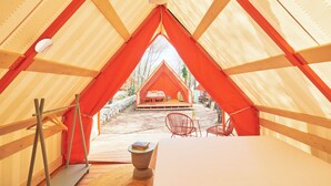 A tent with a bed, a table, and chairs, and a view of a house outside. - LAVITA Camp - Cagliari Villasimius (Quartu Sant'Elena)
