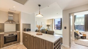 A modern kitchen with a central island, built-in oven, and stainless steel range hood. - Designer Foreshore Apartment | No Loadshedding (Cape Town)