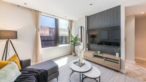 A modern living room with a sofa, a coffee table, a TV, and a large window with curtains. - Designer Foreshore Apartment | No Loadshedding (Cape Town)