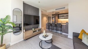 A modern living room with a sofa, coffee table, and a large mirror. There is a dining area with bar stools and a kitchen in the background. - Designer Foreshore Apartment | No Loadshedding (Cape Town)