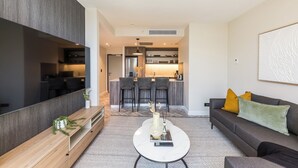 A modern living room with a sofa, coffee table, and a dining area with chairs and a kitchen in the background. - Designer Foreshore Apartment | No Loadshedding (Cape Town)