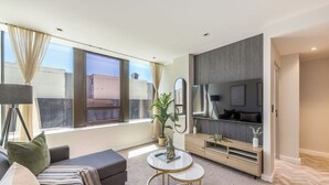 Een moderne woonkamer met een bank, een salontafel, een televisie en een groot raam met gordijnen.