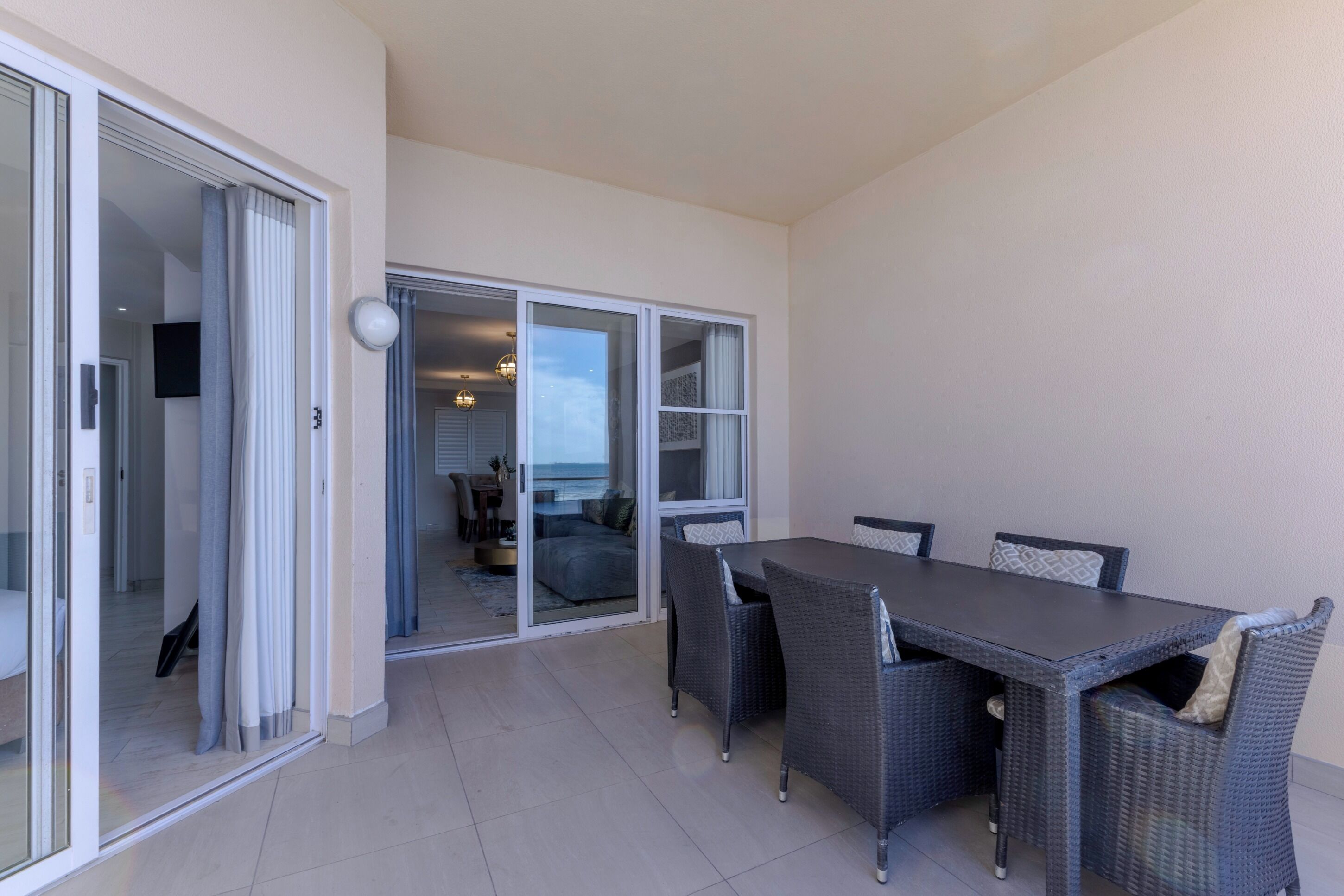 Un balcon avec une table et des chaises pour prendre les repas, une porte-fenêtre coulissante donnant sur une chambre, et une vue sur l’océan.
