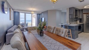 A modern living space with a dining area, kitchen, and a view of the sea. - Lagoon Beach Escape with Breathtaking Views (Cape Town)