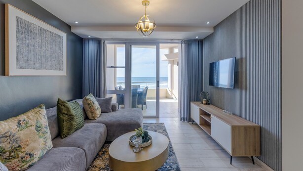 A modern living room with a sofa, coffee table, and a TV on the wall. - Lagoon Beach Escape with Breathtaking Views (Cape Town)