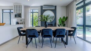 A modern dining area with a large table and six chairs, a round mirror, and a potted plant. - Three Bedroom Family Haven  Sea Point (Cape Town)
