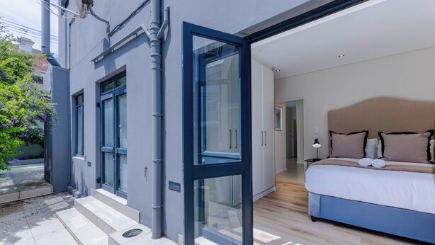 A modern bedroom with a large bed, a glass door leading to a balcony, and a view of the outside. - Three Bedroom Family Haven  Sea Point (Cape Town)