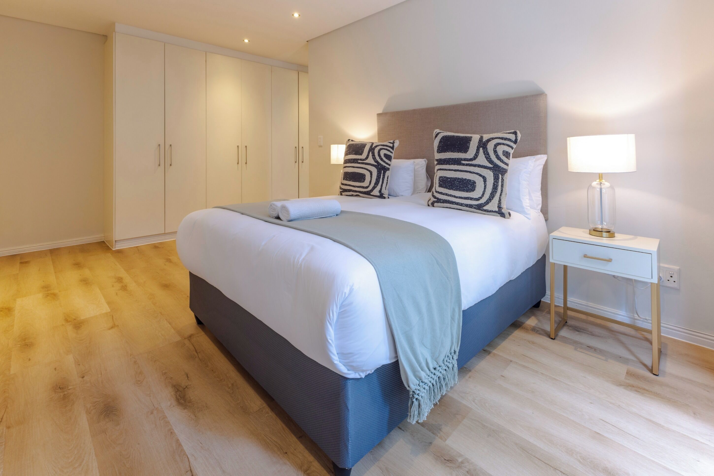Een slaapkamer met een groot bed, een nachtkastje met een lamp en een kledingkast.