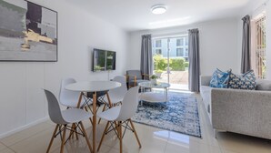 A modern living room with a dining area, a sofa, and a TV on the wall. - 2-Bedroom Family Retreat in Gardens | Pool (Cape Town)