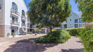 A courtyard with a paved walkway, a large tree, and a building with balconies and windows. - 2-Bedroom Family Retreat in Gardens | Pool (Cape Town)