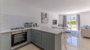 A modern kitchen with a gas stove, oven, and microwave. There is a dining area with a table and chairs, and a view of the outdoors through a sliding glass door. - 2-Bedroom Family Retreat in Gardens | Pool (Cape Town)