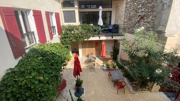 Un patio con mobiliario exterior, un muro de piedra y un edificio con contraventanas rojas.