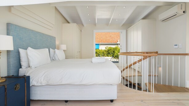 A bedroom with a large bed, a nightstand, a dresser, and a staircase leading to an outdoor area.