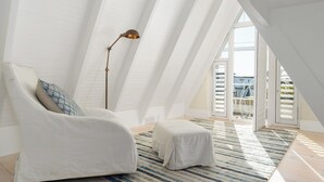 A modern loft bedroom with a sloped ceiling, a large window, a white sofa, a floor lamp, and a striped rug.